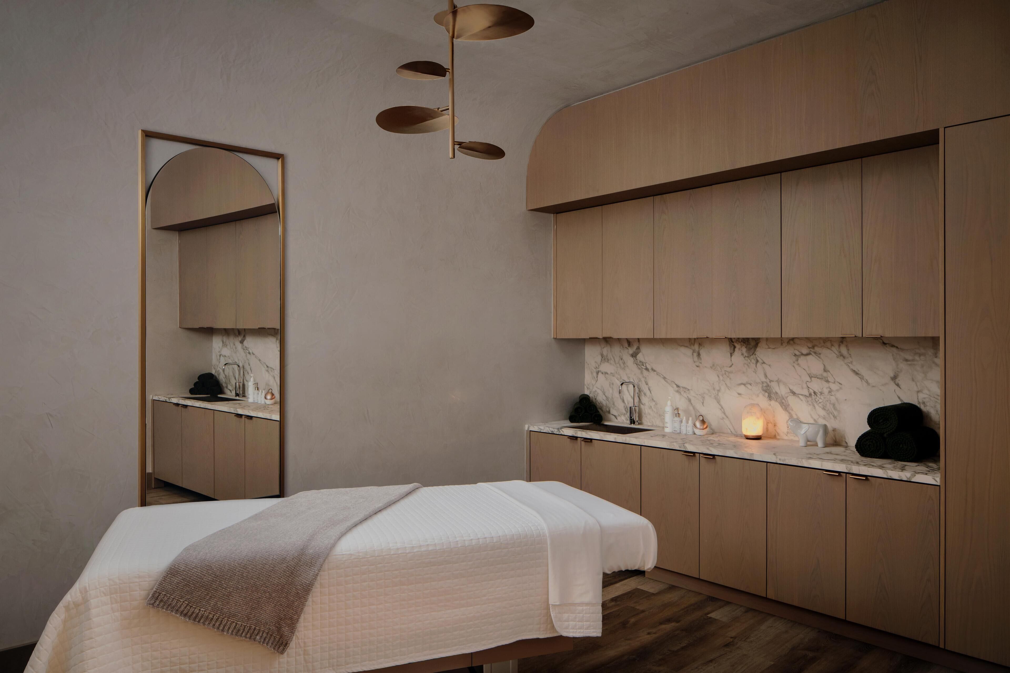 A modern bathroom with a large mirror, wooden cabinets, a marble countertop, and a bed with a blanket.