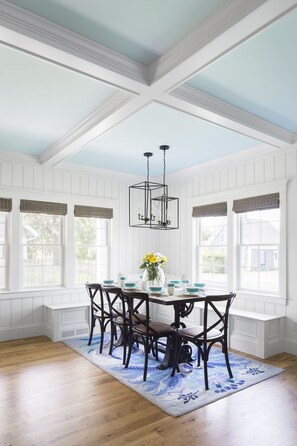 Enjoy meals in this elegant dining area with a high ceiling, set with a table and chairs, and adorned with a vase and decorative bowls.