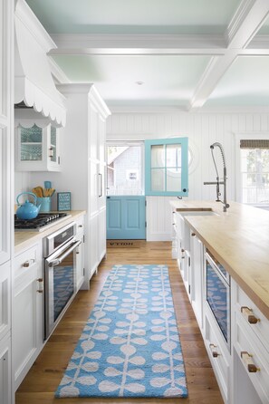 Une cuisine avec des meubles blancs, une porte bleue et un tapis à motifs bleus.