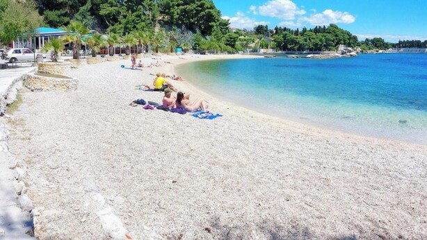 Ein Strand mit Personen, die sonnenbaden, und einer blauen Struktur auf der linken Seite.