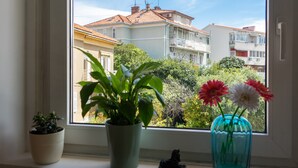 Ein Fenster mit Blick auf Gebäude, ein Blumentopf und eine Vase mit Blumen.