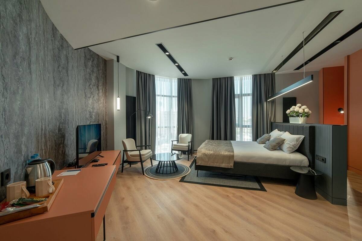 A modern hotel room with a large bed, a desk with a computer, a chair, and a TV.