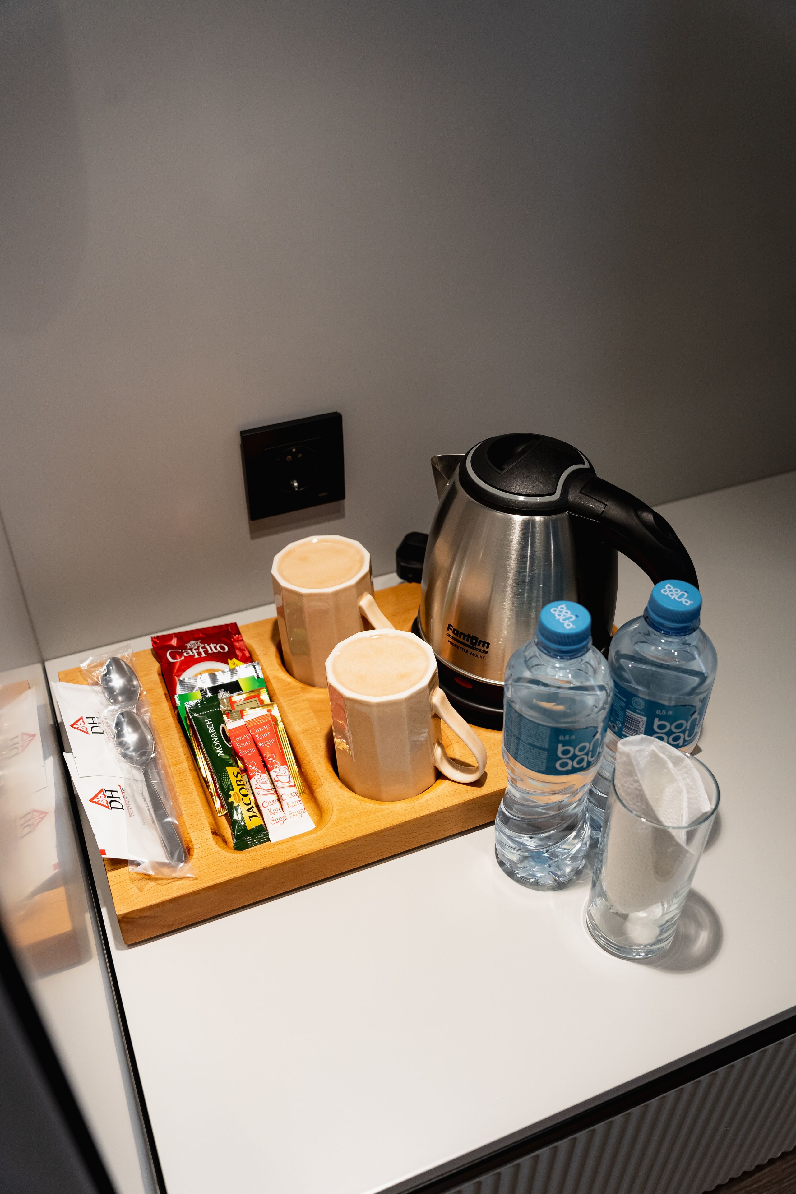A breakfast tray with a coffee maker, two mugs, a packet of biscotti, a bottle of water, and a glass of milk on a hotel counter.