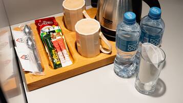 A breakfast tray with a coffee maker, two mugs, a packet of biscotti, a bottle of water, and a glass of milk on a hotel counter.