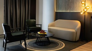 Een moderne woonkamer met een bank, twee fauteuils, een salontafel met fruit, een vloerlamp en een groot abstract kunstwerk aan de muur.