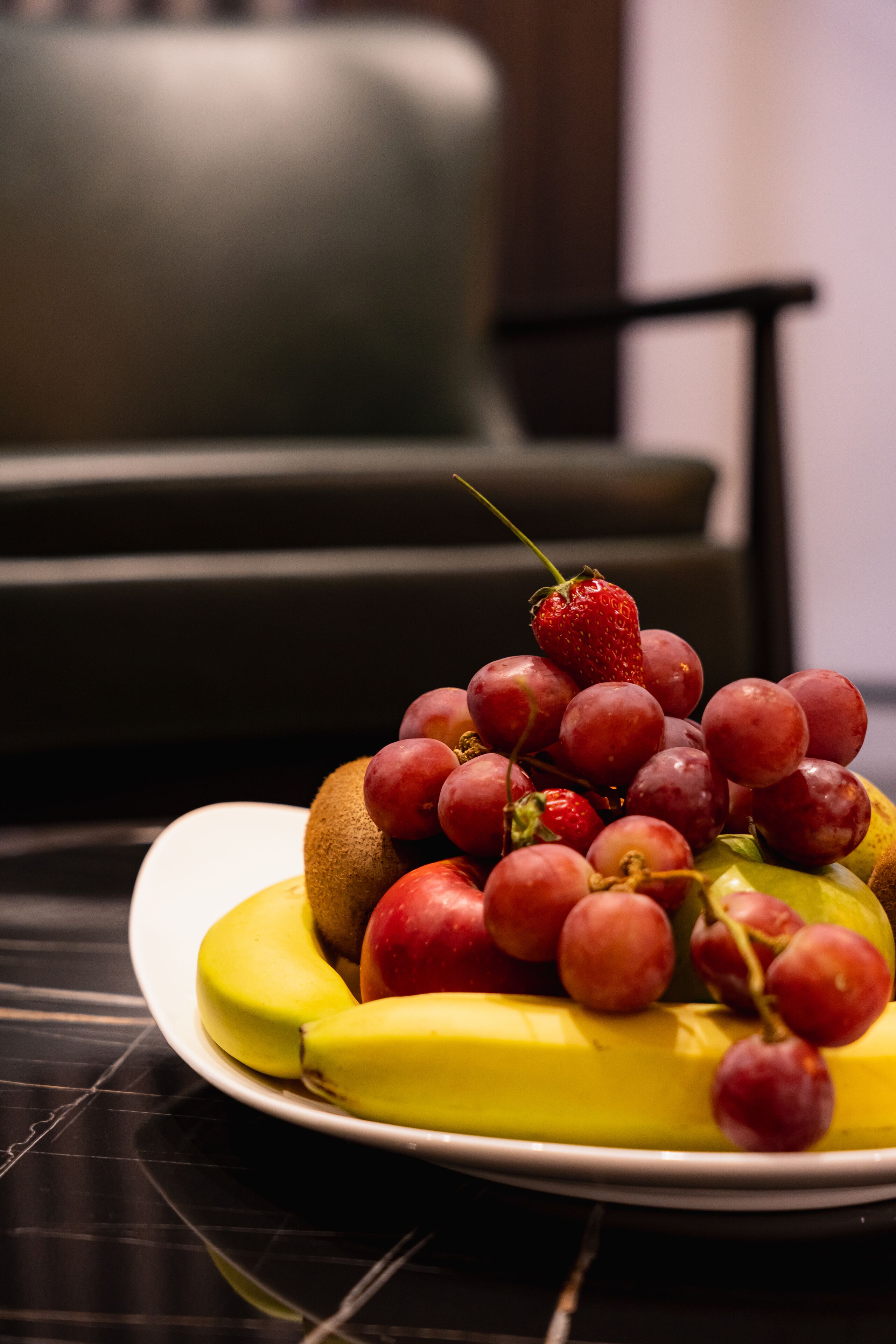 A plate of fruit including bananas, grapes, and a strawberry on a table.