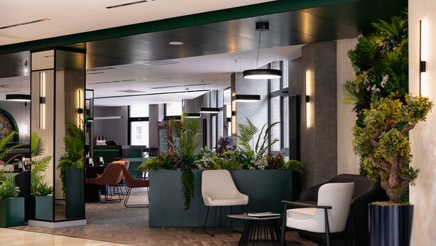 Een moderne lobby met een receptiebalie, een zithoek en binnenplanten.
