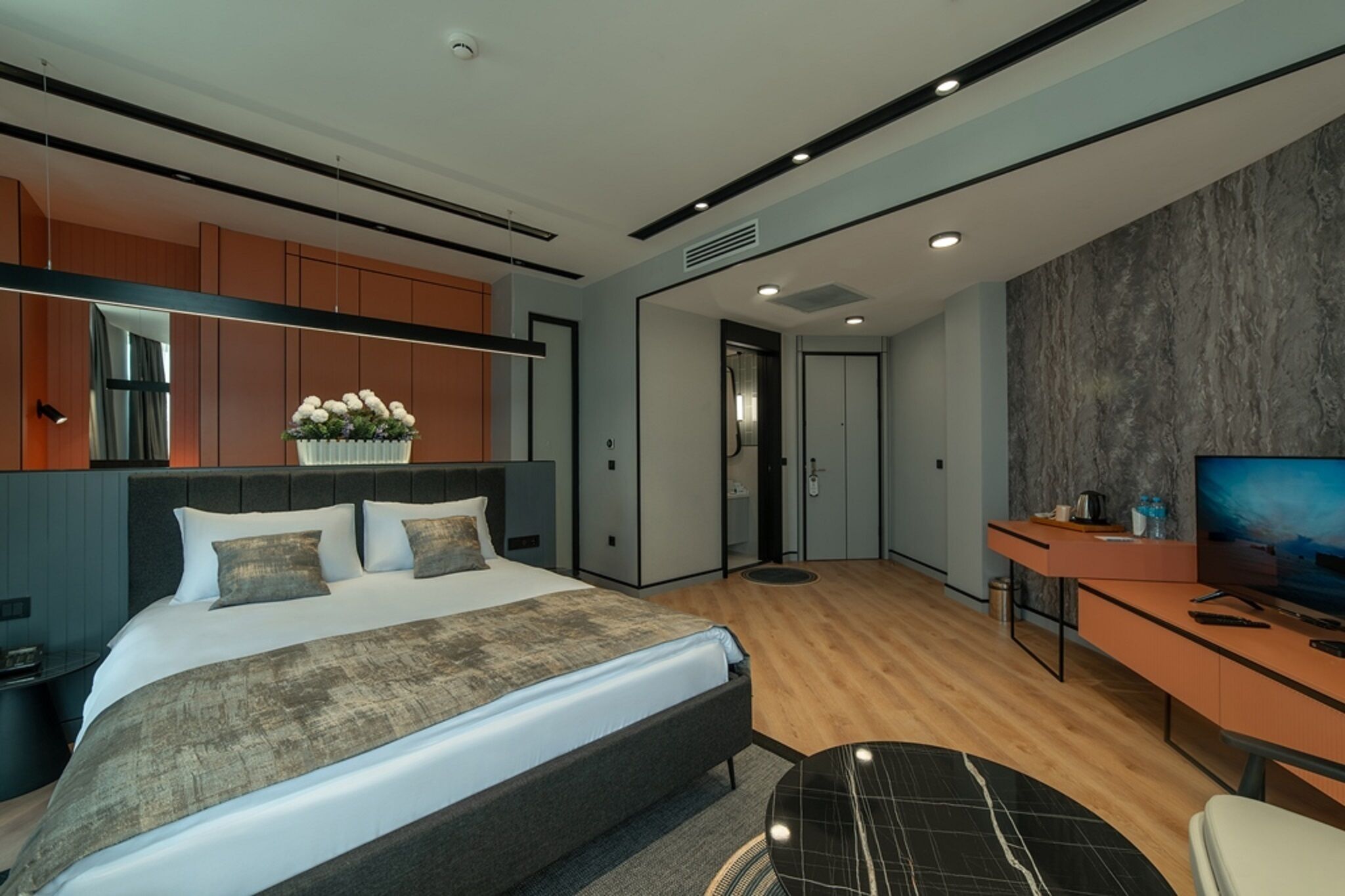 A modern hotel room with a large bed, a desk, a television, and a bathroom.
