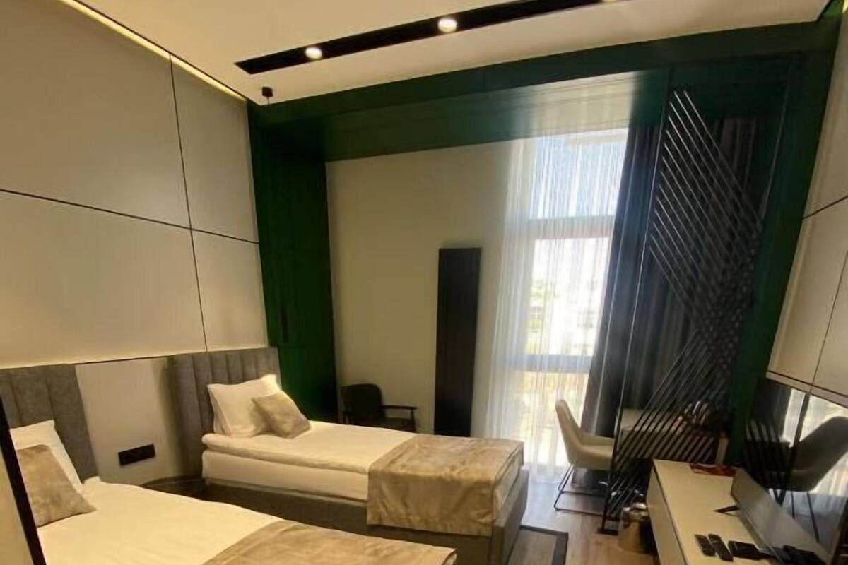 A modern hotel room with two beds, a desk, and a large window.