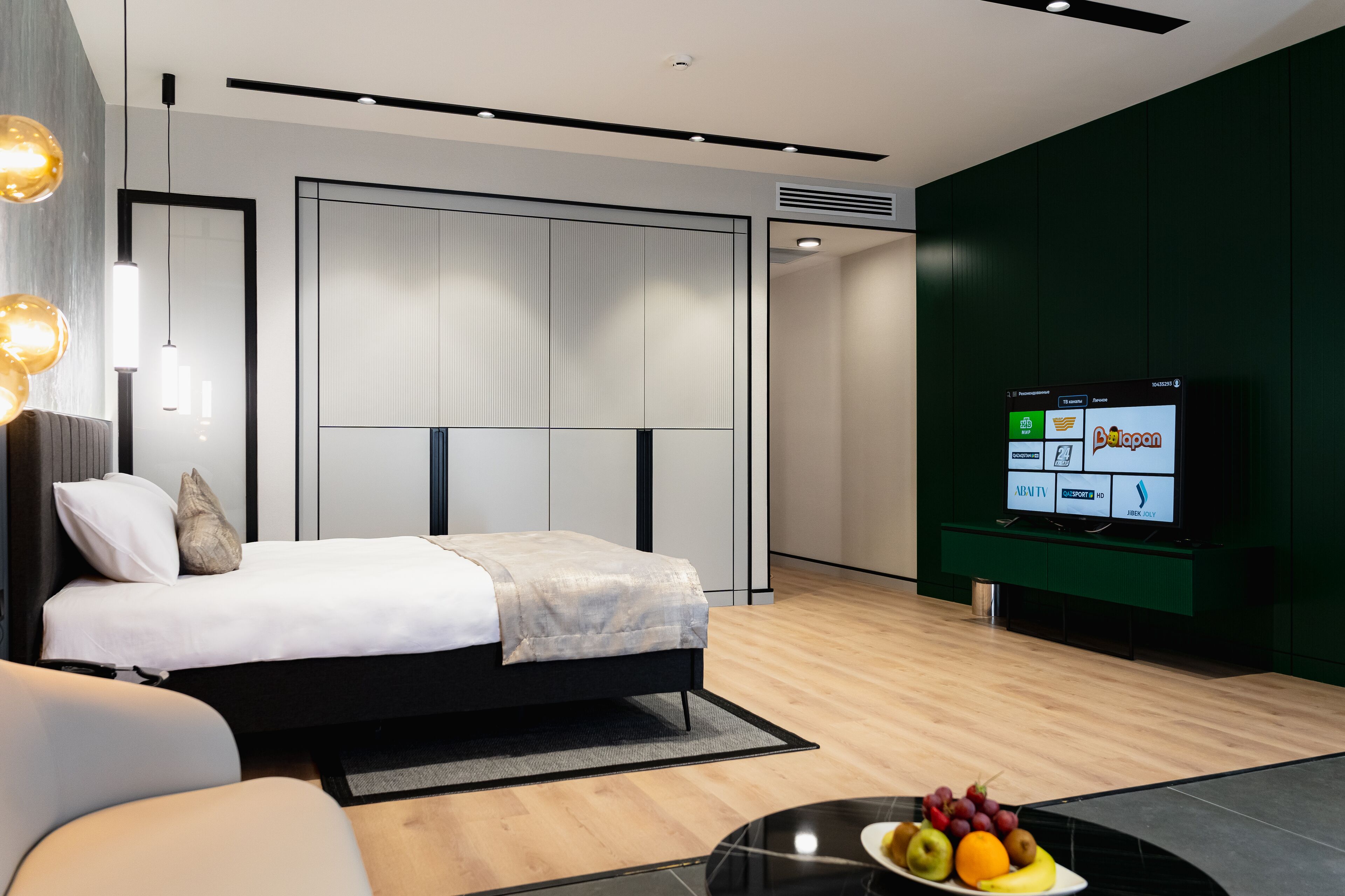 A modern hotel room with a bed, a television displaying a program, and a fruit bowl on a table.
