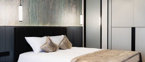 A modern bedroom with a black bed, a wooden floor, and a textured wall.