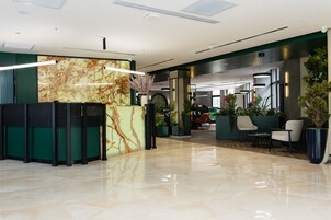 A modern lobby with a marble reception desk, green seating area, and indoor plants.