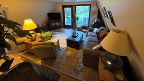 A living room with a sofa, a coffee table, a TV, and a lamp. - Mountain Bliss is a quiet mountain retreat, sleeps 6, hot tub, pet friendly (Evergreen)