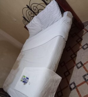 Un matelas recouvert de draps blancs, un petit autocollant dans le coin inférieur gauche et un sol à motifs.
