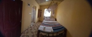 Un couloir étroit avec un lit au fond, une petite table avec une chaise et une porte sur la gauche.