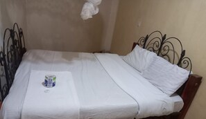 Un lit bien fait, avec du linge de lit blanc et un petit récipient posé sur le pied de lit.
