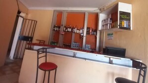Zona de bar con mostrador, taburetes y estanterías llenas de botellas y latas.