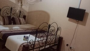 Un dormitorio con cama, televisor montado en la pared y mosquitero colgando sobre la cama.