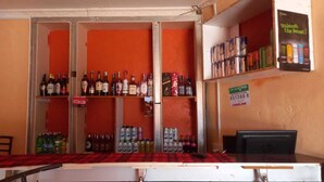 Una zona de bar con estantes llenos de botellas y latas, una barra con mantel a cuadros y un cartel que indica un precio de 8.13 dólares.