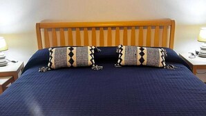 Ein Schlafzimmer mit einem hölzernen Kopfteil, einem großen Bett mit einer dunkelblauen Steudecke und zwei gemusterten Kissen. An der Wand hängt ein gerahmtes Bild eines Bootes.