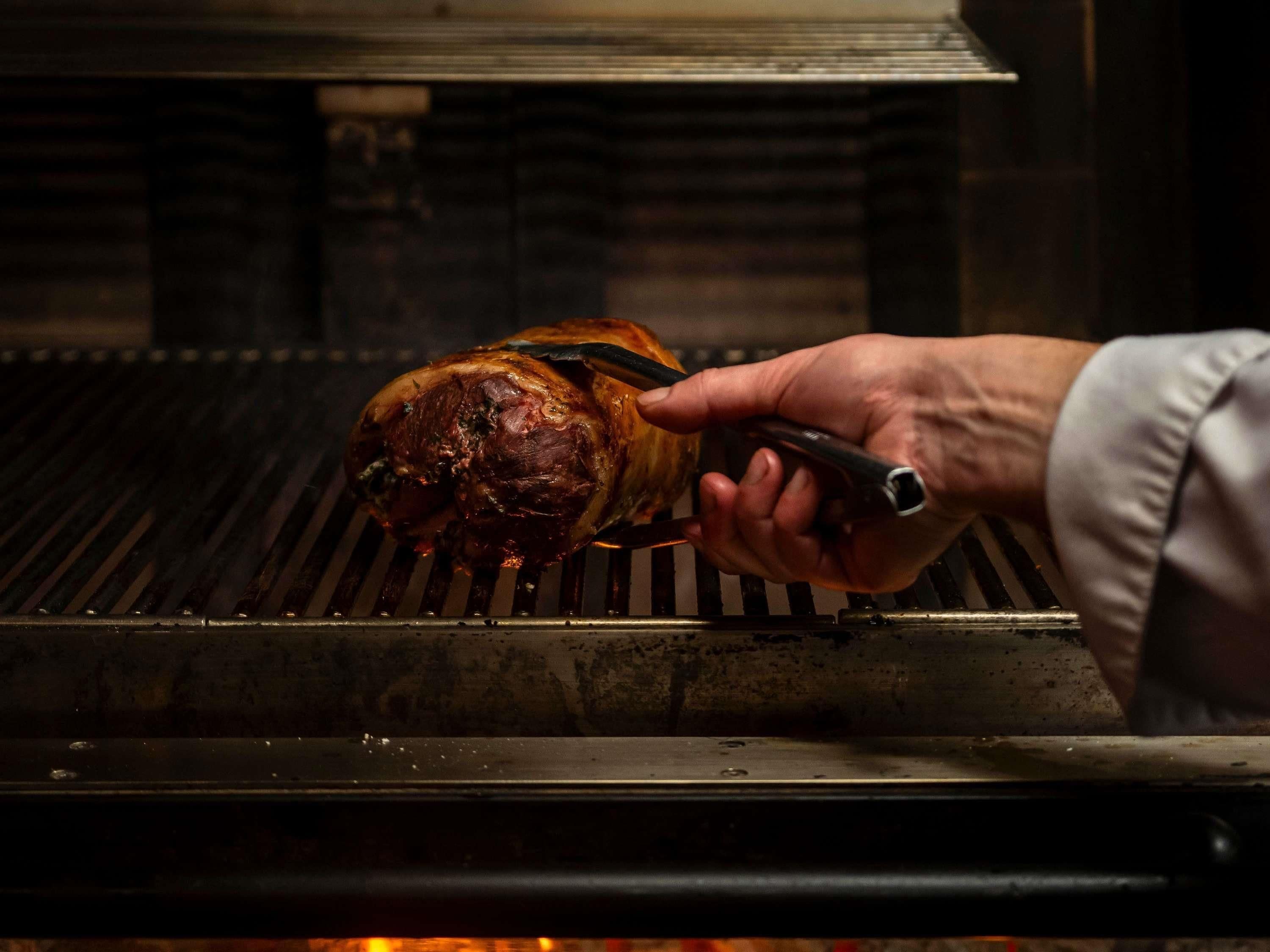 Una mano usando pinzas para manipular carne asada en una parrilla.