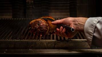 Una mano usando pinzas para manipular carne asada en una parrilla.