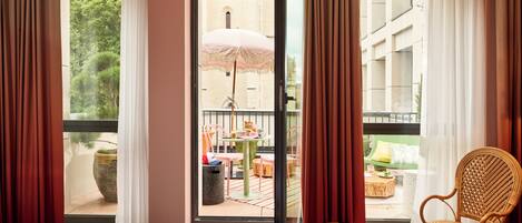 Ein Hotelzimmer mit großem Fenster, einem Korbstuhl, einem kleinen Tisch und einem Bett.