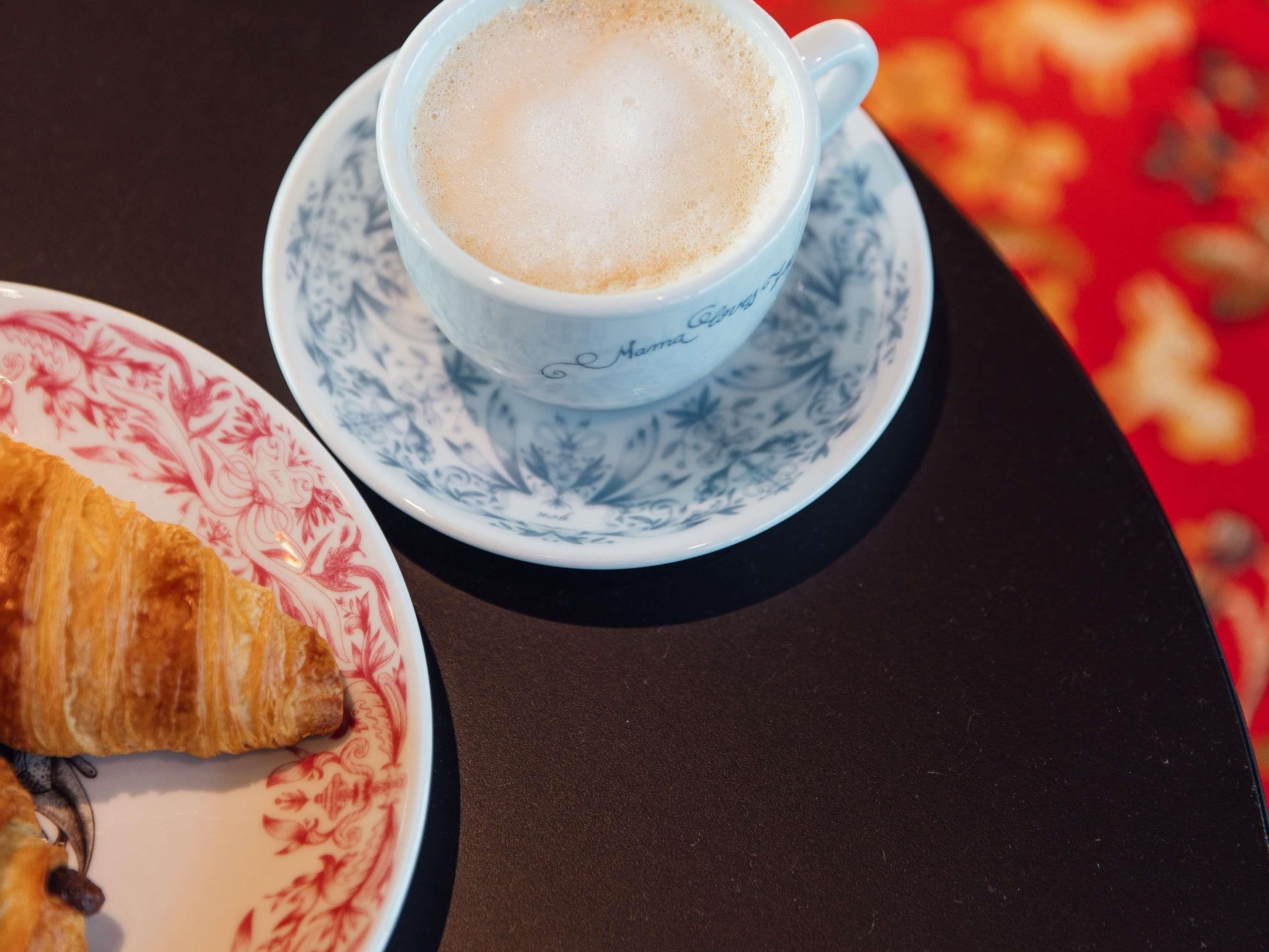 Uma chávena de café sobre um pires com um croissant num prato.