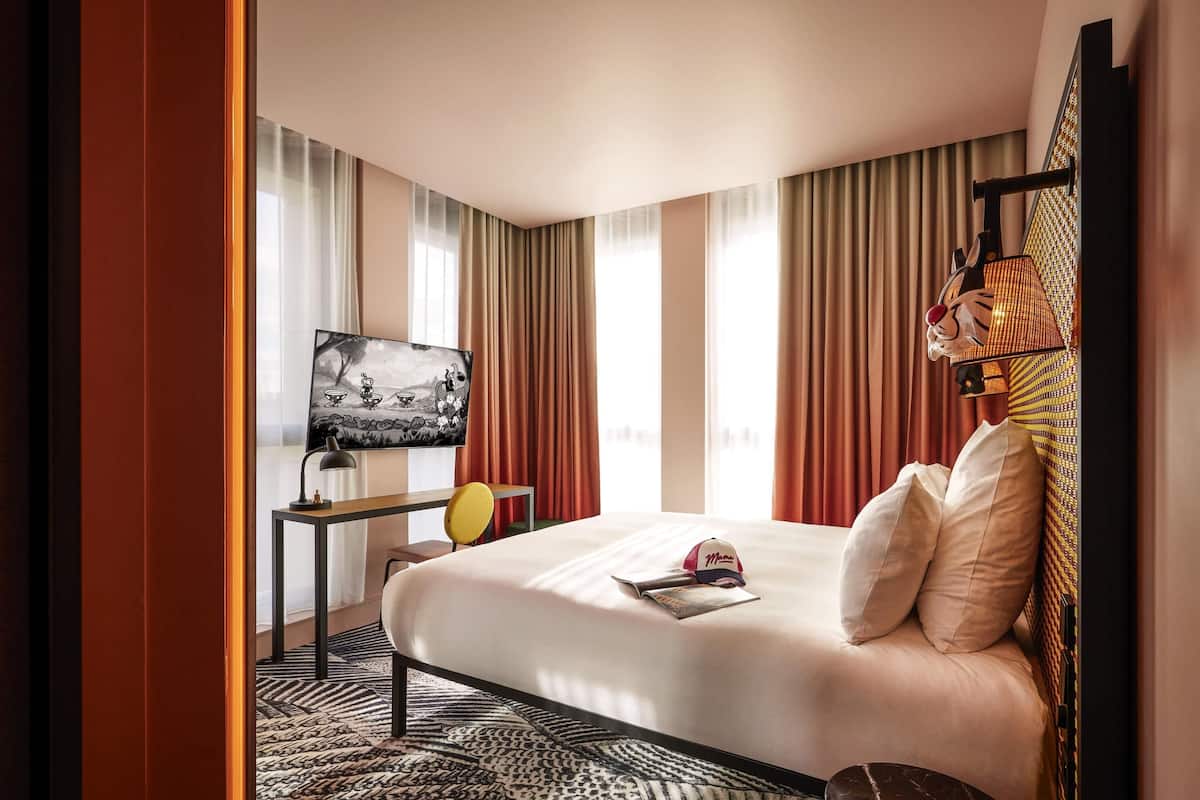 A hotel room with a bed, a desk with a chair, a television, and curtains.