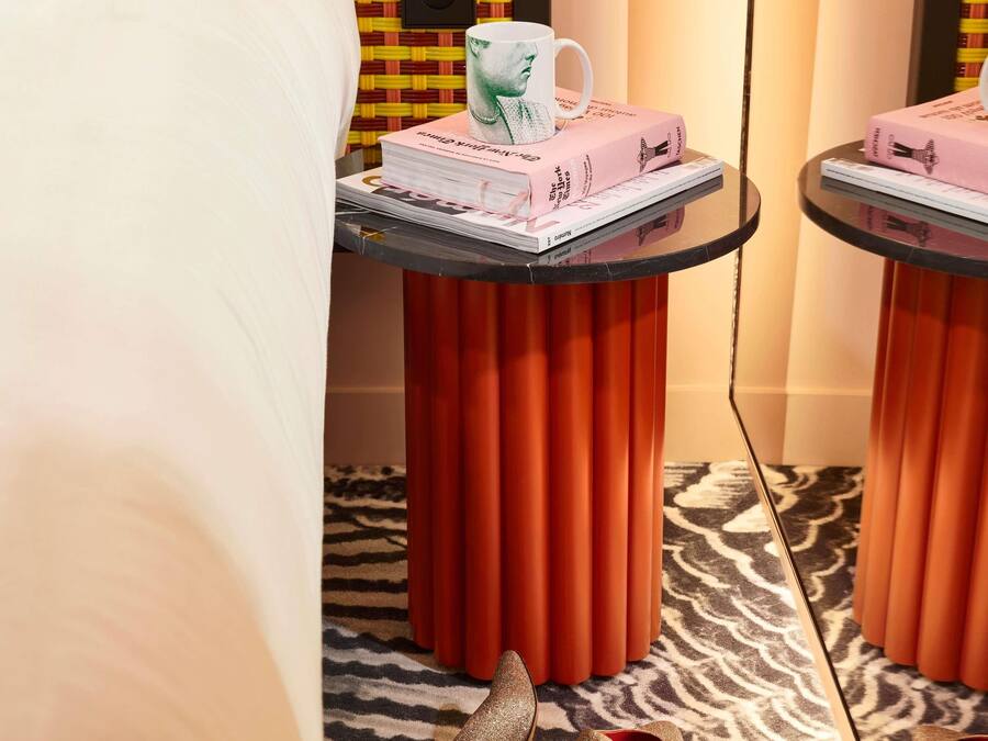 Una habitación con una alfombra estampada con diseño de cebra, una mesa con una pila de libros y una taza, y un par de zapatos en el suelo.