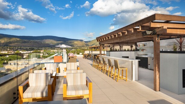 A rooftop terrace with outdoor seating, a bar area, and a view of the surrounding landscape.