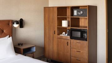 A hotel room with a bed, a wooden wardrobe, a bedside table with a lamp, and a microwave.