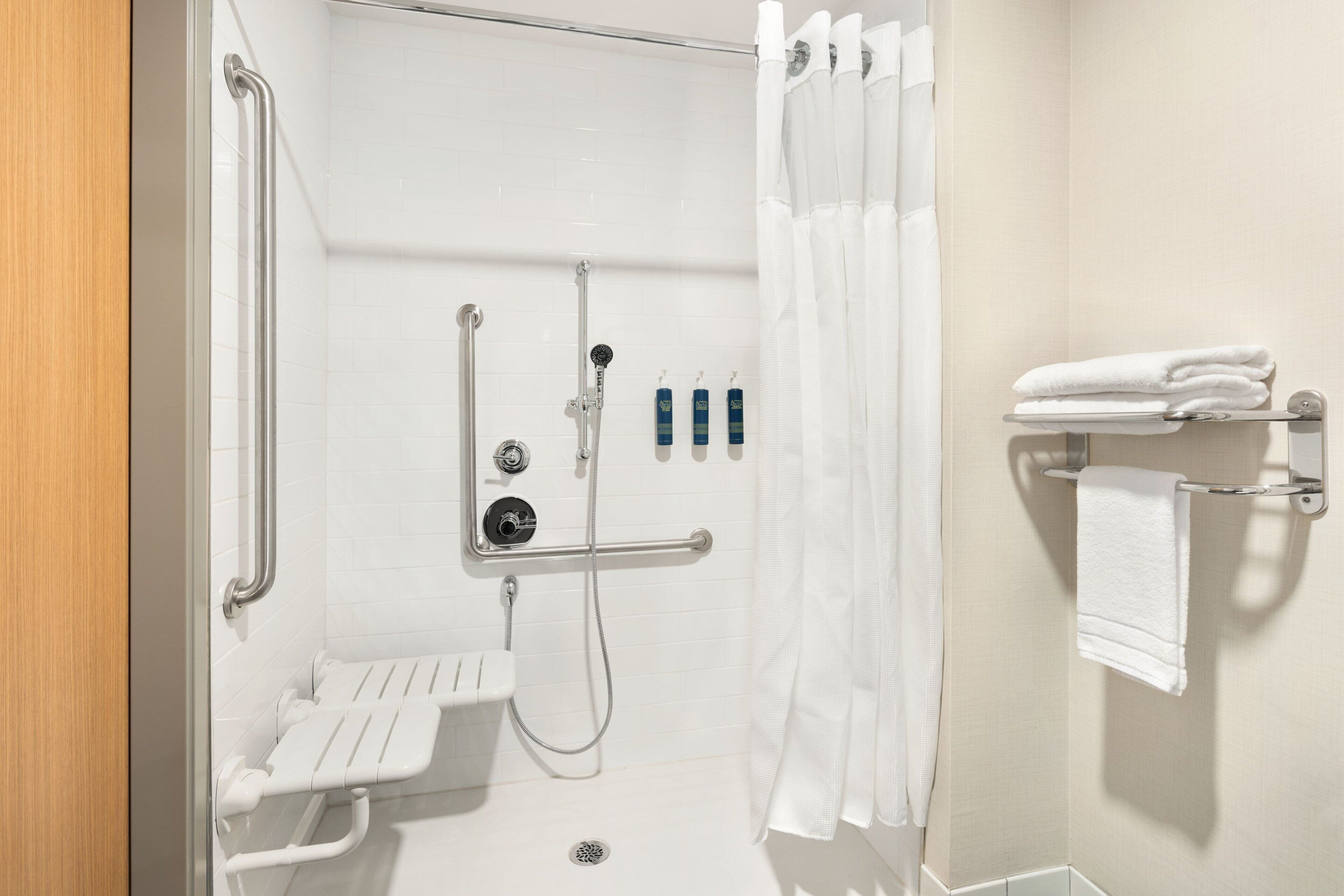 A shower area with a grab bar, a bench, a towel rack, and a showerhead.