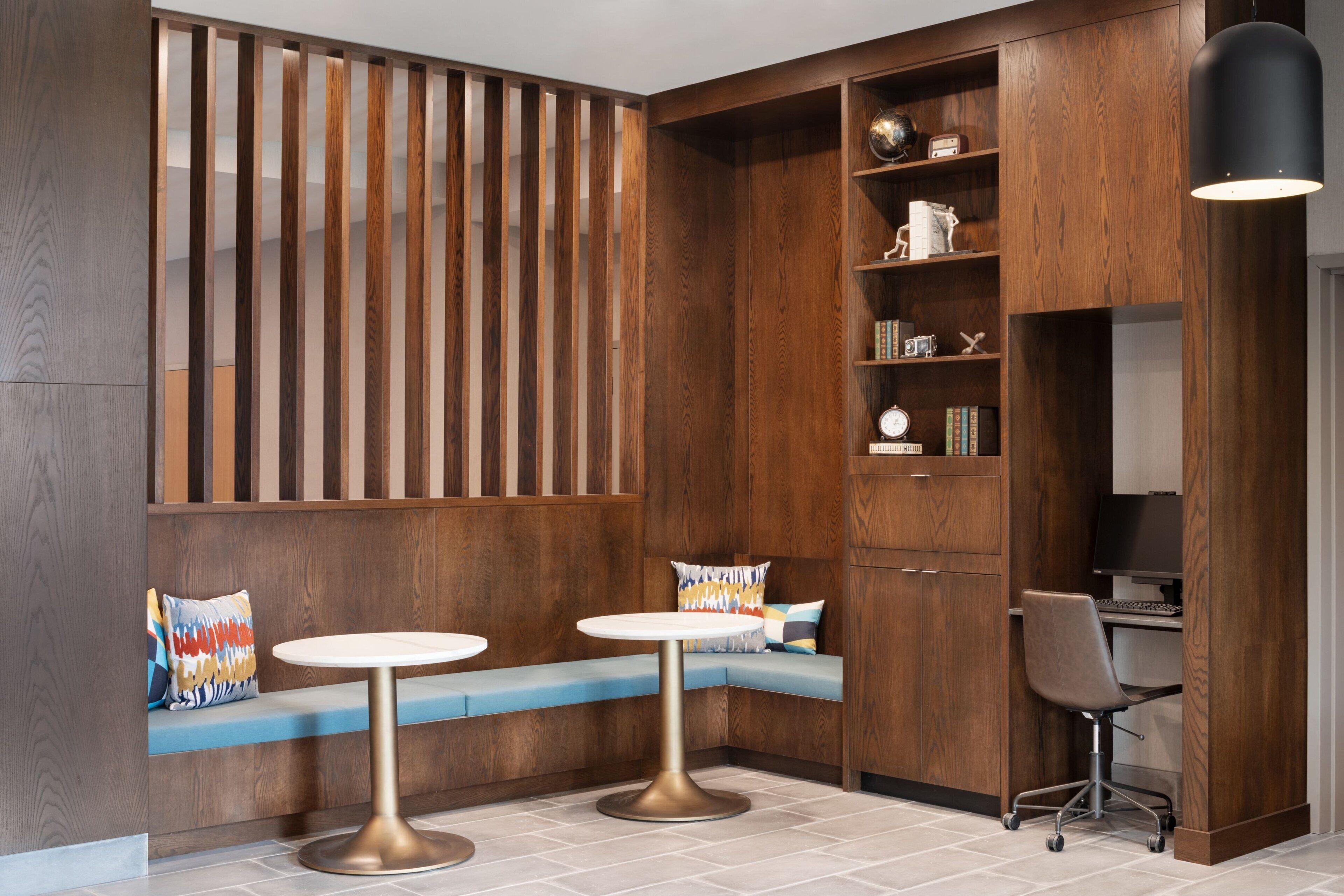 A modern room with a wooden partition, two round tables, a bench with cushions, and a desk with a chair.