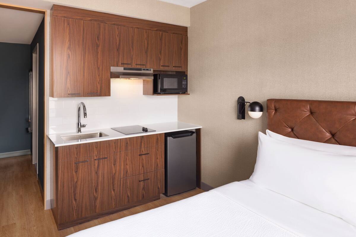 A compact hotel room with a kitchenette, including a microwave, sink, and dishwasher.
