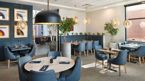 A modern dining area with round tables, blue chairs, and pendant lighting.