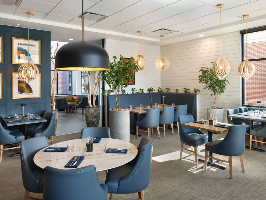 Un comedor moderno con mesas redondas, sillas azules e iluminación colgante.