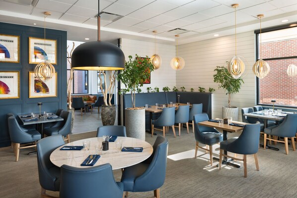 Een moderne eetruimte met ronde tafels, blauwe stoelen en hanglampen.