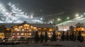 Un chalet doté d’une grande entrée illuminée et d’une piste de ski en arrière-plan.