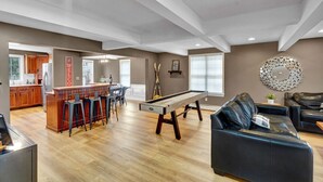 Un grand espace de vie comprenant une table de billard, un bar avec des tabourets, un canapé et une cuisine à l’arrière-plan.