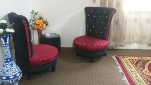 A corner of a room with two black upholstered chairs with red cushions, a blue and white patterned vase with flowers, and a small table with a vase of orange flowers. - Banjosa Inn Guest House (Chhota Gala)