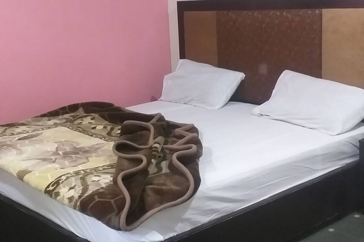 Uma cama de solteiro com um cobertor estampado, uma cabeceira e um tapete verde com pontos brancos.