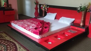 A bed with a red and white bedspread, two white pillows, and a red headboard. There are two red bedside tables with vases of flowers. - Banjosa Inn Guest House (Chhota Gala)