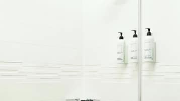 A shower with a handheld showerhead, a glass door, and toiletries on a shelf.