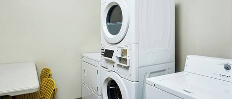 A laundry room with stacked washers and dryers, a table, and chairs.
