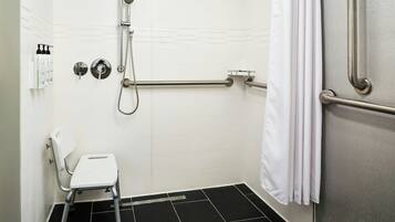 A bathroom with a shower, grab bars, a white chair, and a towel rack.
