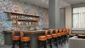 A bar area with a wall of liquor bottles, bar stools, and a seating area with a patterned rug. - SpringHill Suites by Marriott New York Queens (Long Island City)