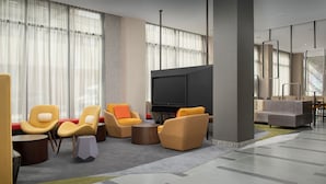 A modern hotel lobby with a large flat-screen TV, comfortable seating areas, and a large window with sheer curtains. - SpringHill Suites by Marriott New York Queens (Long Island City)