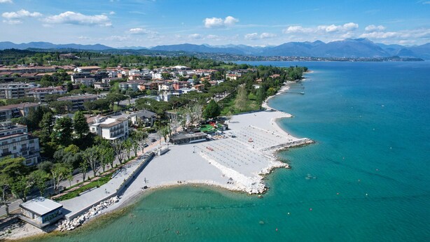 An aerial view of a coastal town with a beach, buildings, and mountains in the background. - DesenzanoLoft Splendido  (Desenzano del Garda)