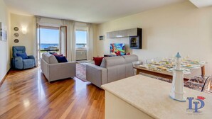 A modern living room with a sofa set, a dining table with chairs, and a view of the sea through large windows. - DesenzanoLoft Splendido  (Desenzano del Garda)